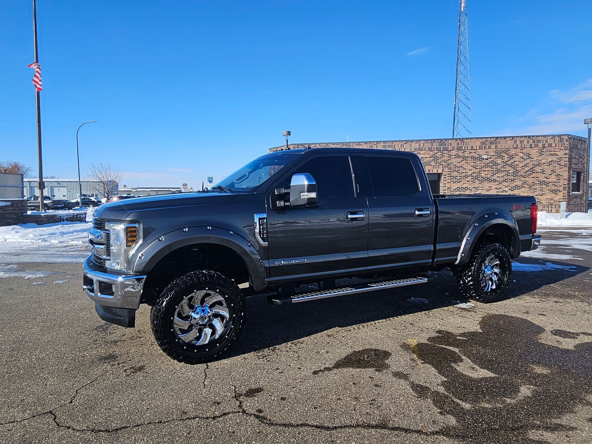 Black lifted pickup truck parked on wet pavement in front of a brick building under a blue sky