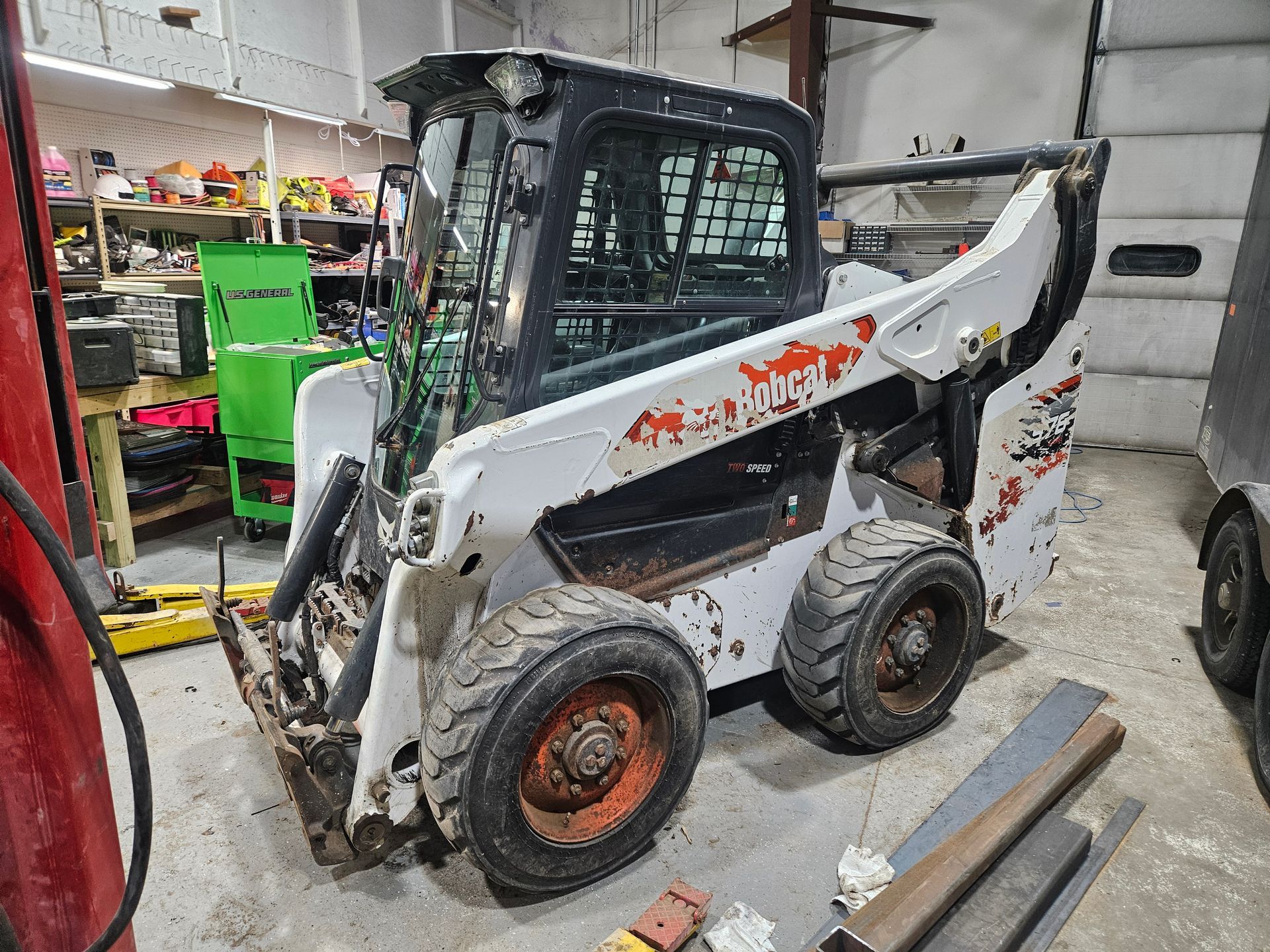 Bobcat skid steer in a workshop, with white body, black cab, and worn orange wheels.