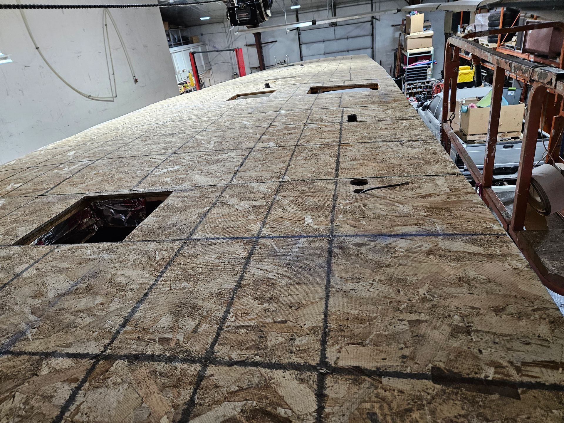 Partially built floor covered in plywood sheets with cutout openings inside a workshop or construction site