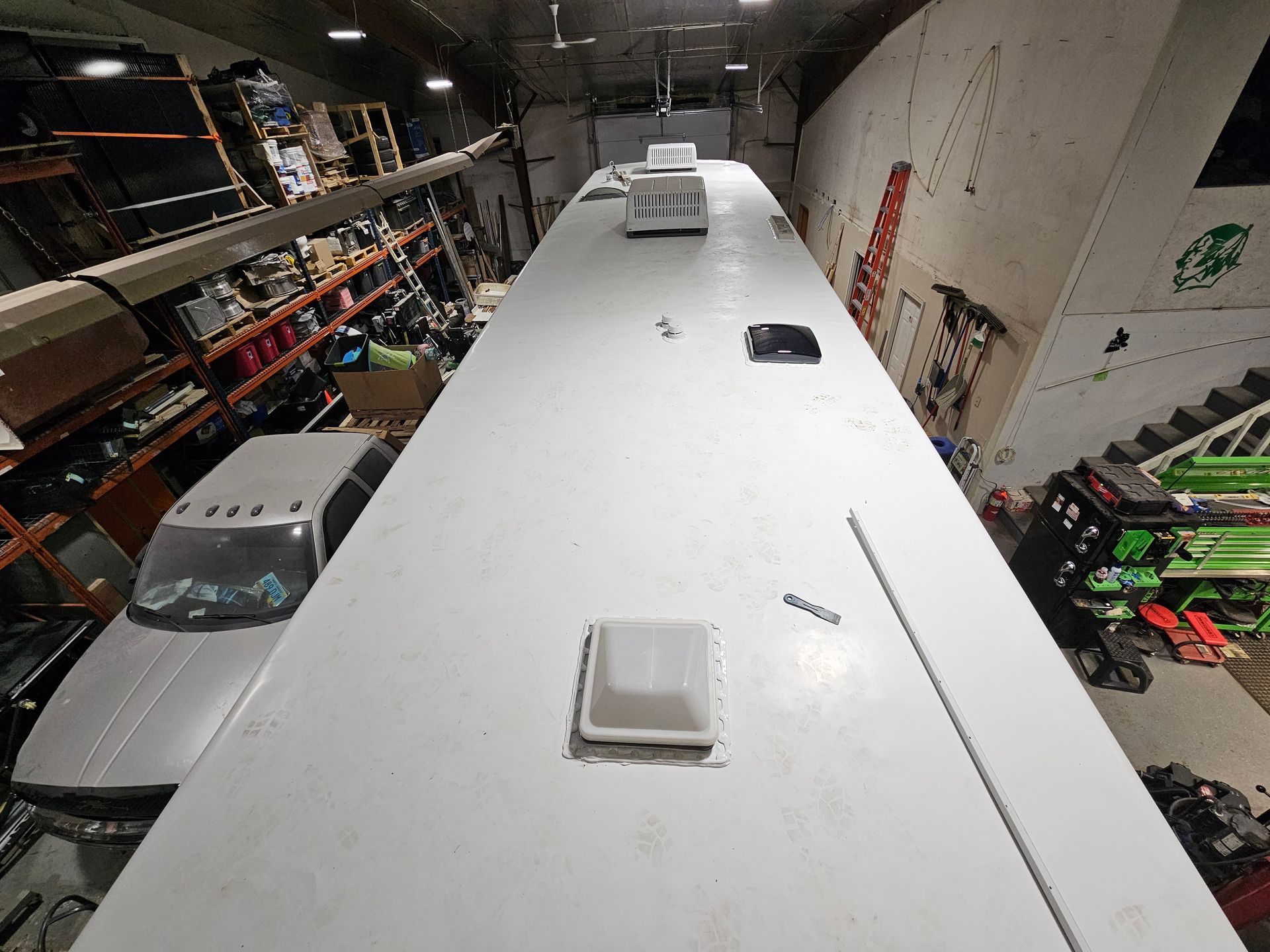 Top view of a white bus roof inside a workshop, with vents and equipment visible on both sides