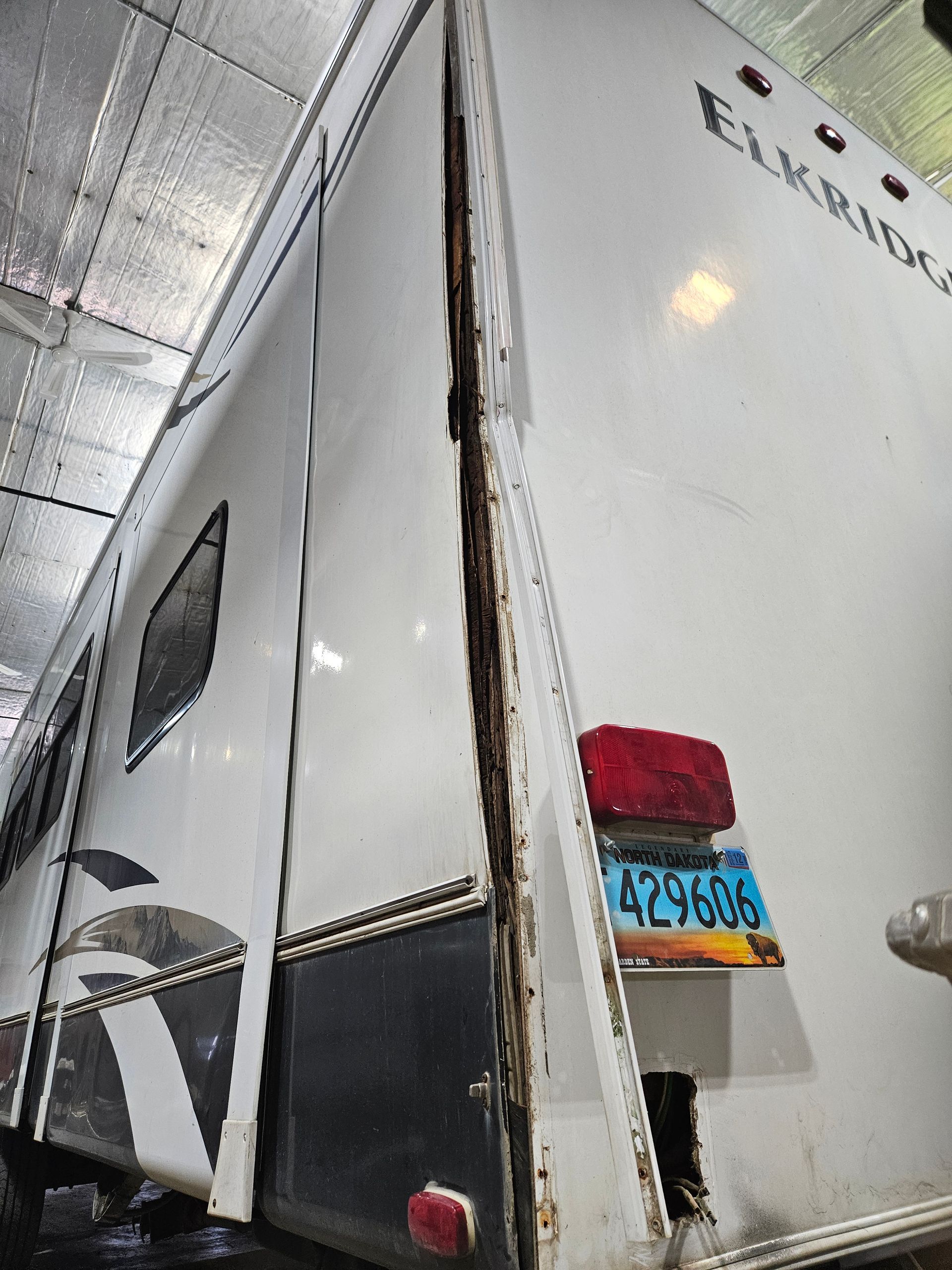 Rear side of a white box truck in a covered area, with a partially open door and a red taillight.
