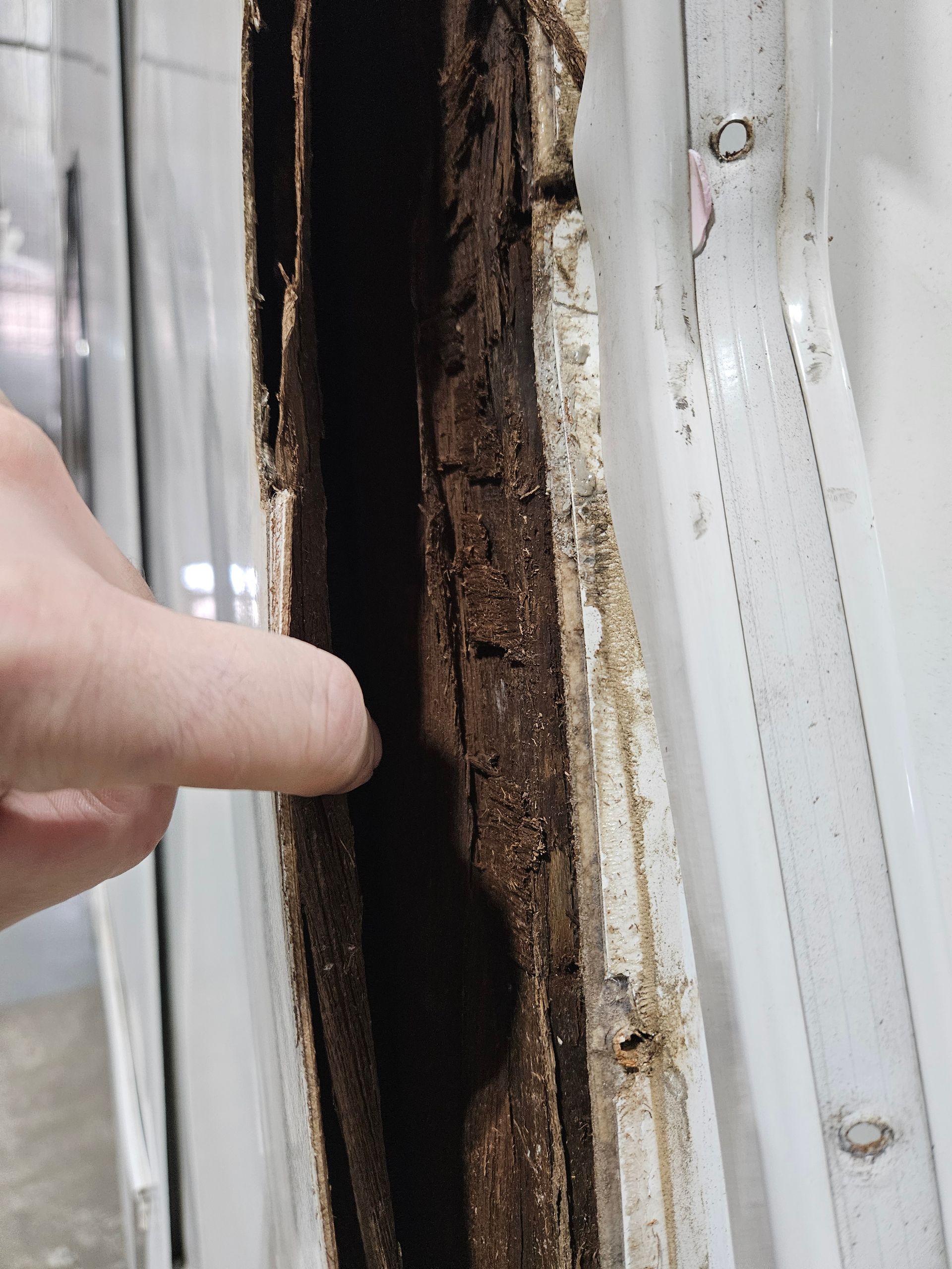 Hand pointing at a damaged, rusted window frame with peeling sealant
