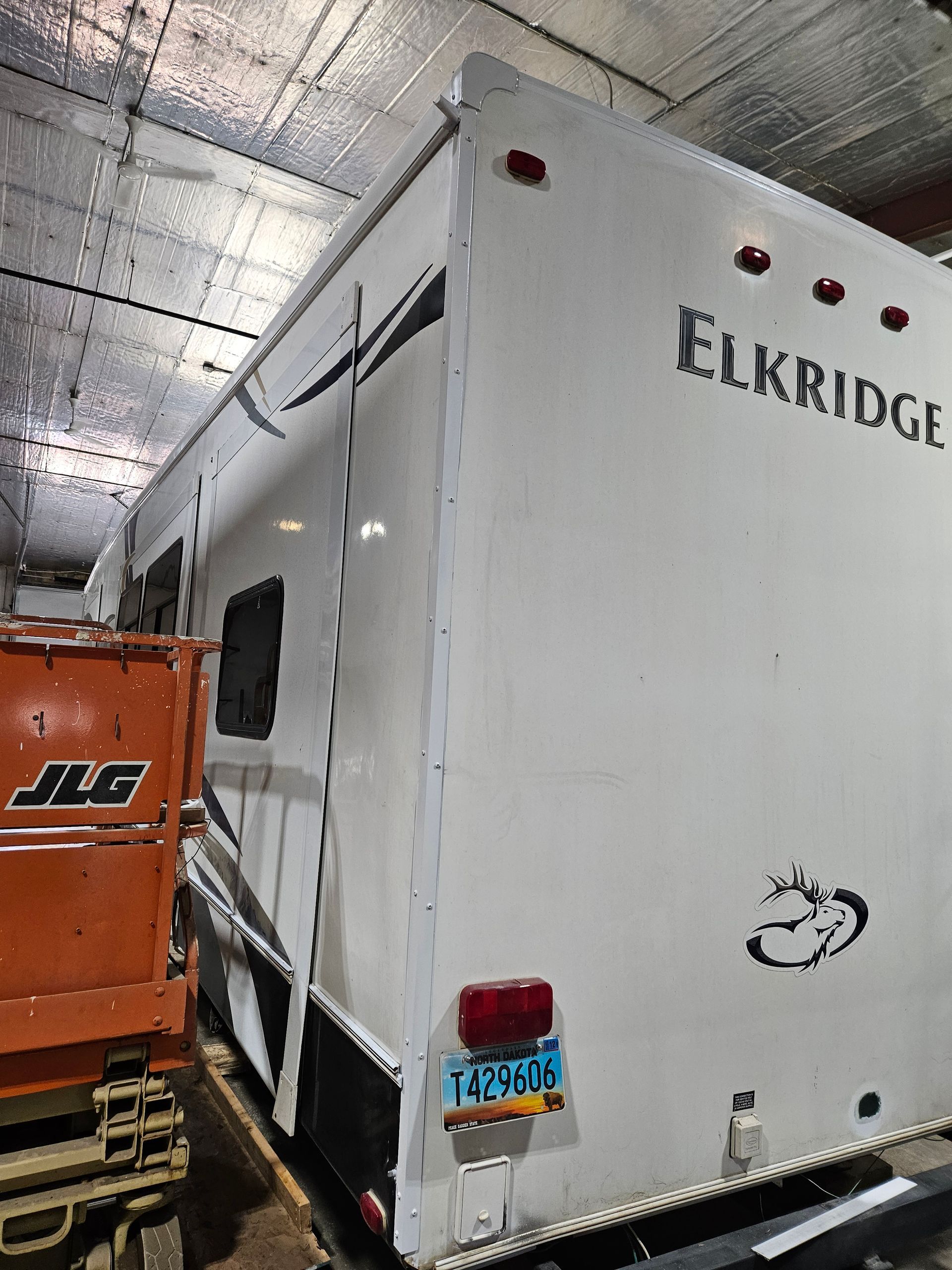 White Elkridge trailer in a warehouse beside an orange truck, rear view
