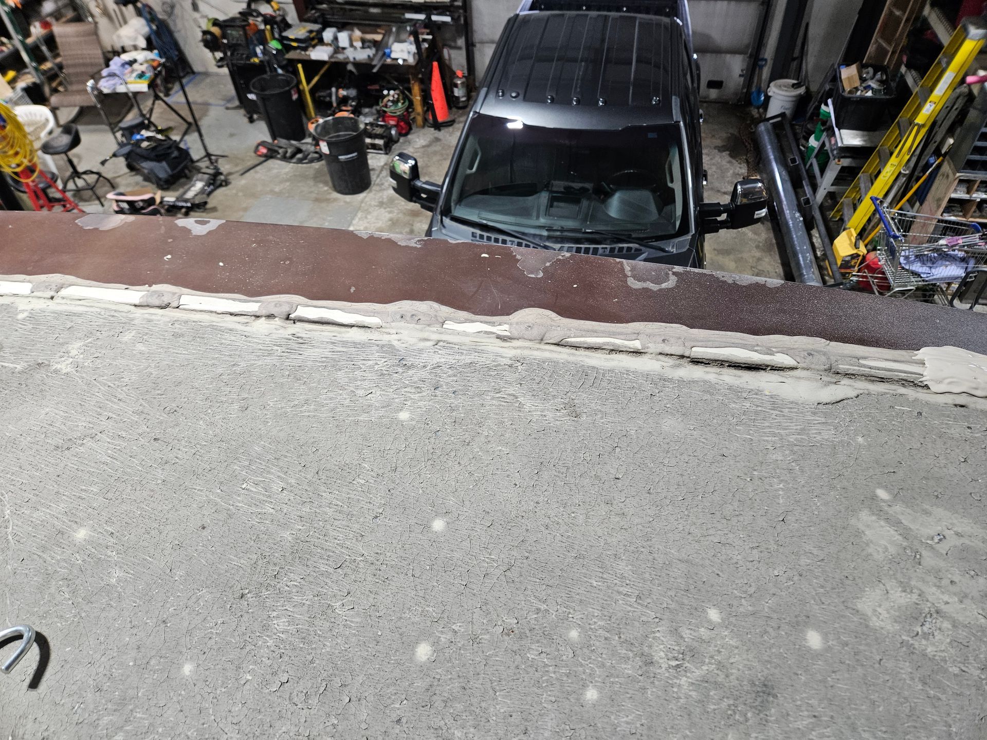 Car parked inside a cluttered garage, viewed from an elevated rooftop edge.
