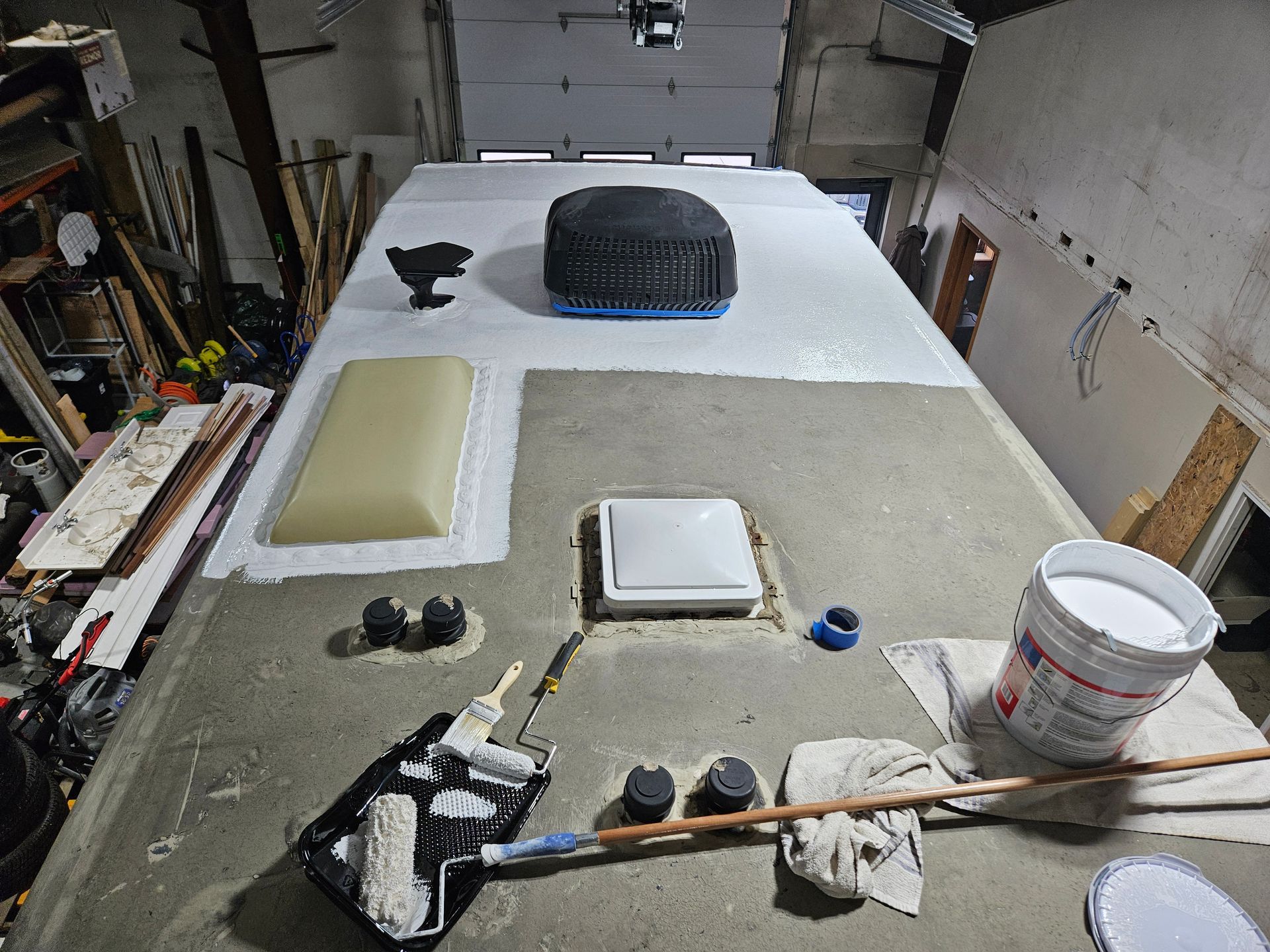 Garage workbench covered with materials, tools, and a large tire on a white surface