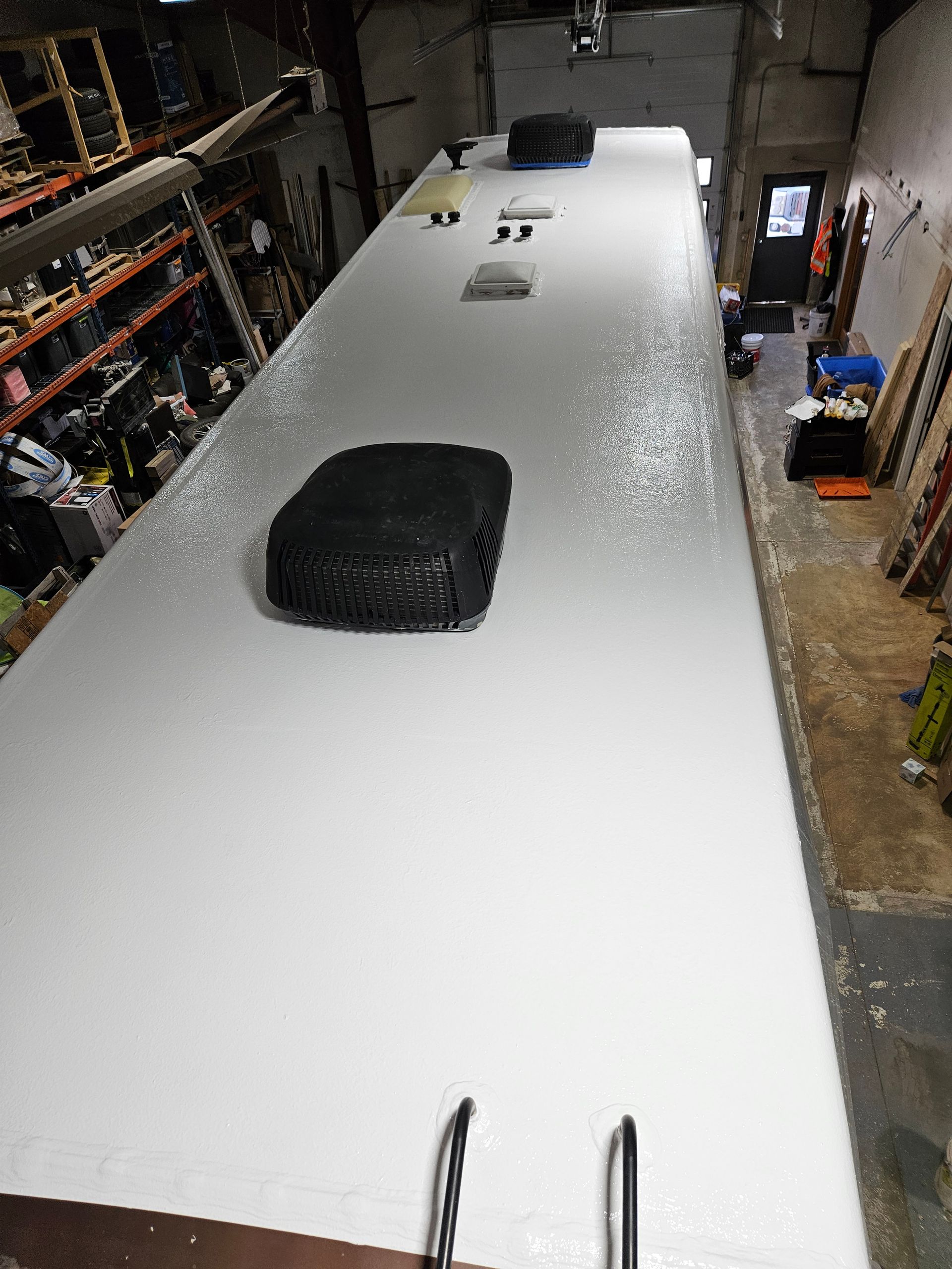White RV roof in a workshop, with vents and skylights visible from above.