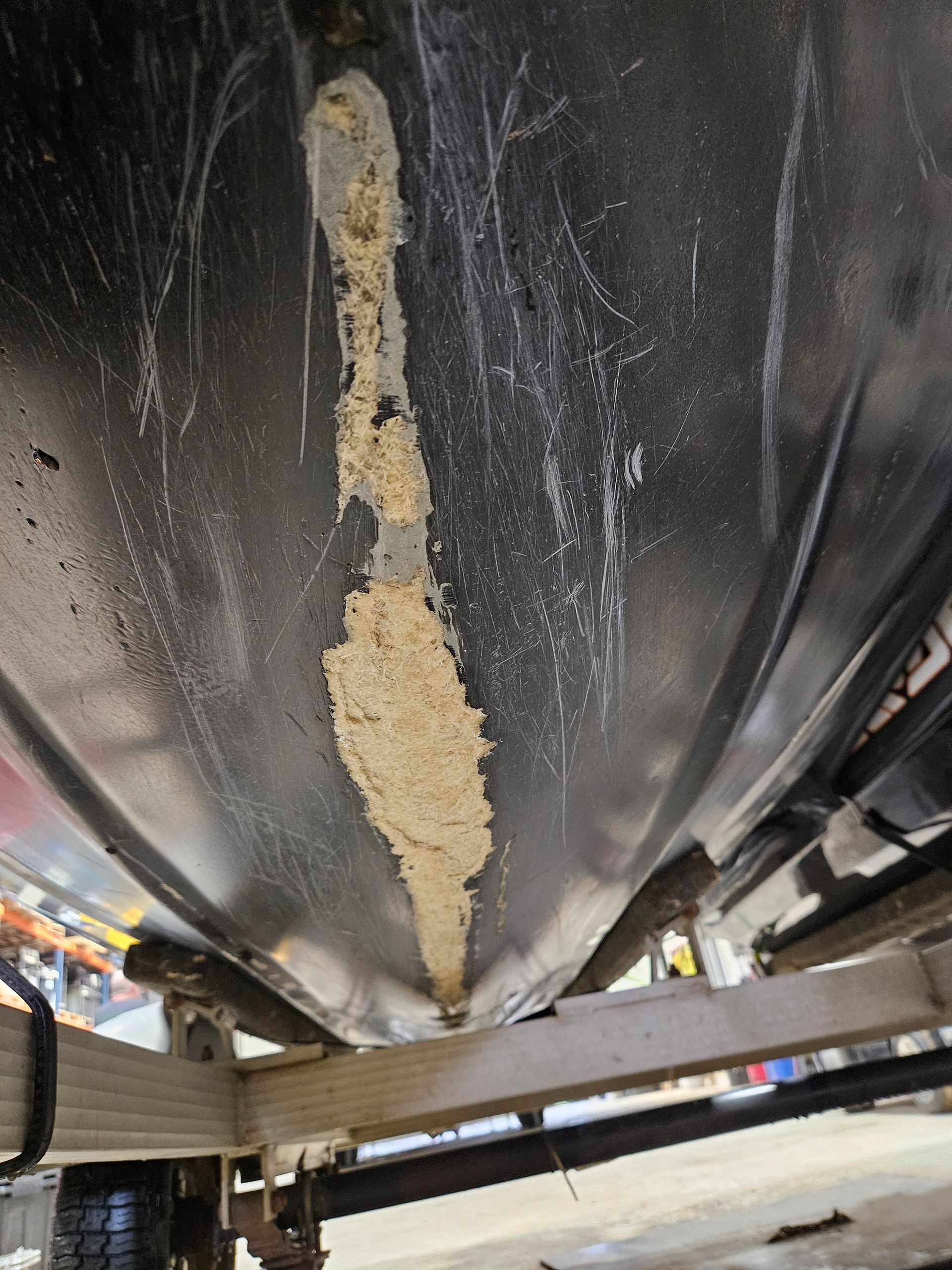 Damaged black underside of a vehicle or tank with a long beige scrape and support rails below