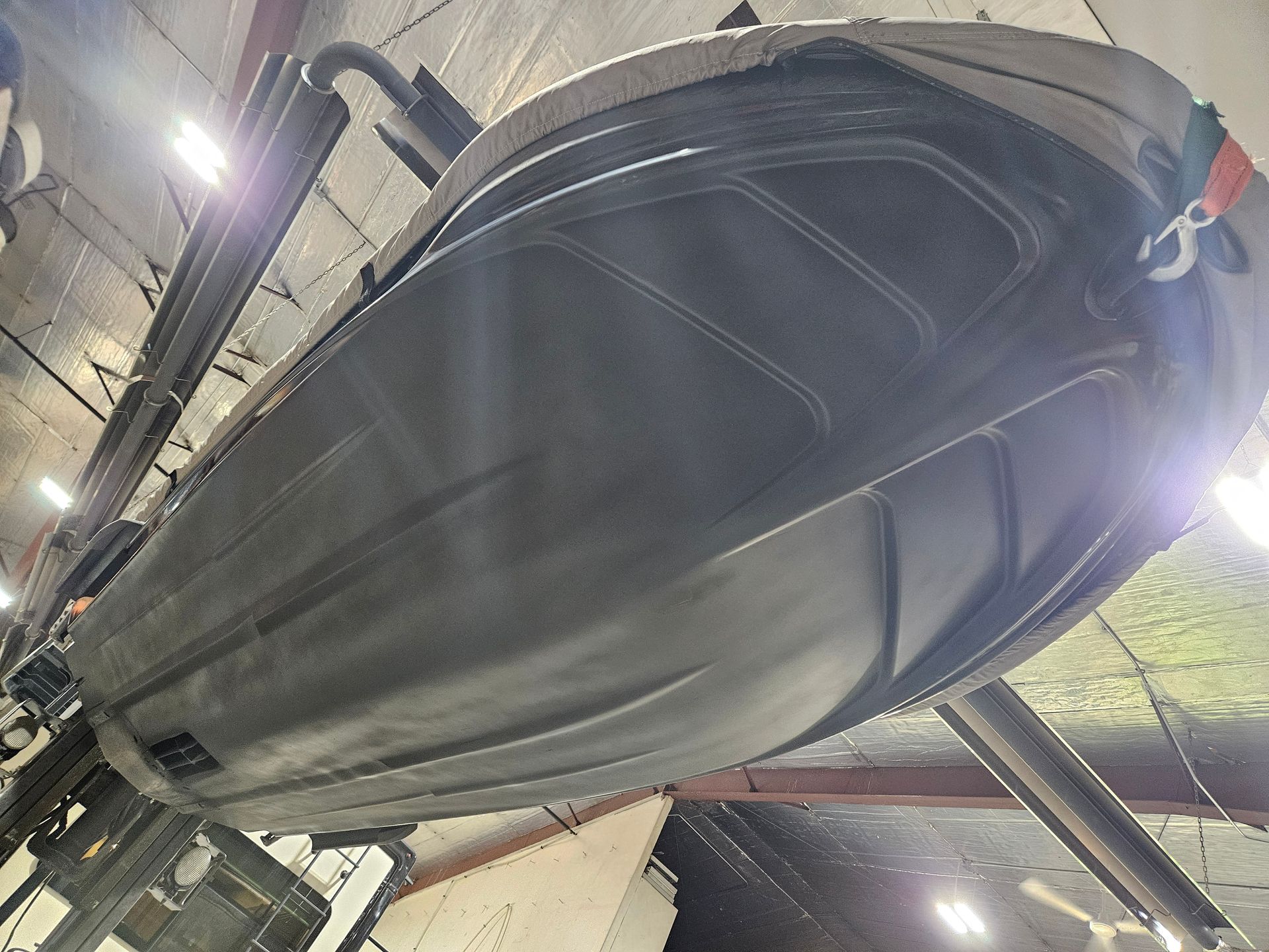 Large black boat hull under construction in a boatyard, viewed from below.