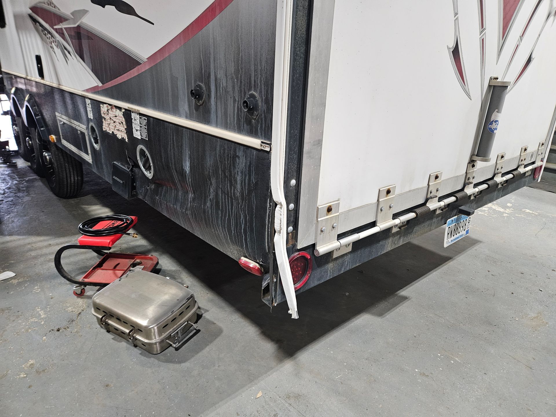 Damaged white trailer with scrape marks, with a suitcase and red bag lying on the pavement nearby.