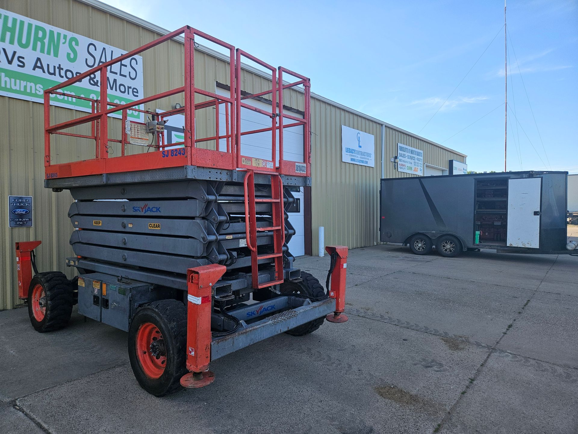 Red scissor lift parked outside a warehouse in an industrial lot under a clear sky