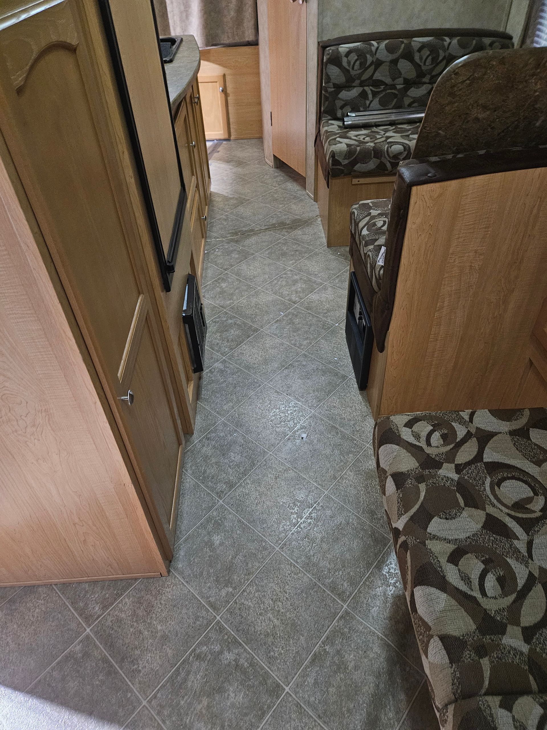 Narrow RV hallway with wood cabinets, patterned seating, and gray tile floor