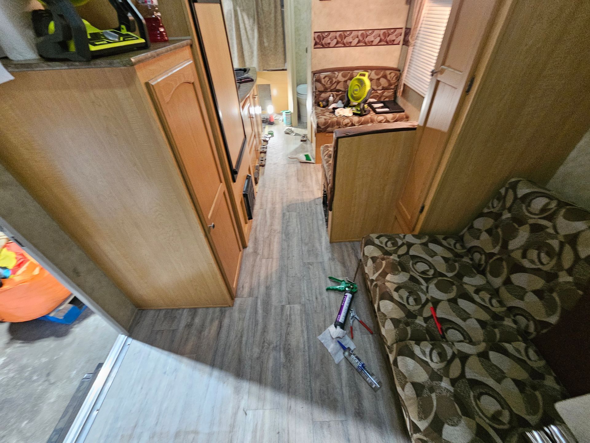 Narrow RV hallway with wood cabinets, patterned sofa, and cluttered floor near the doorway