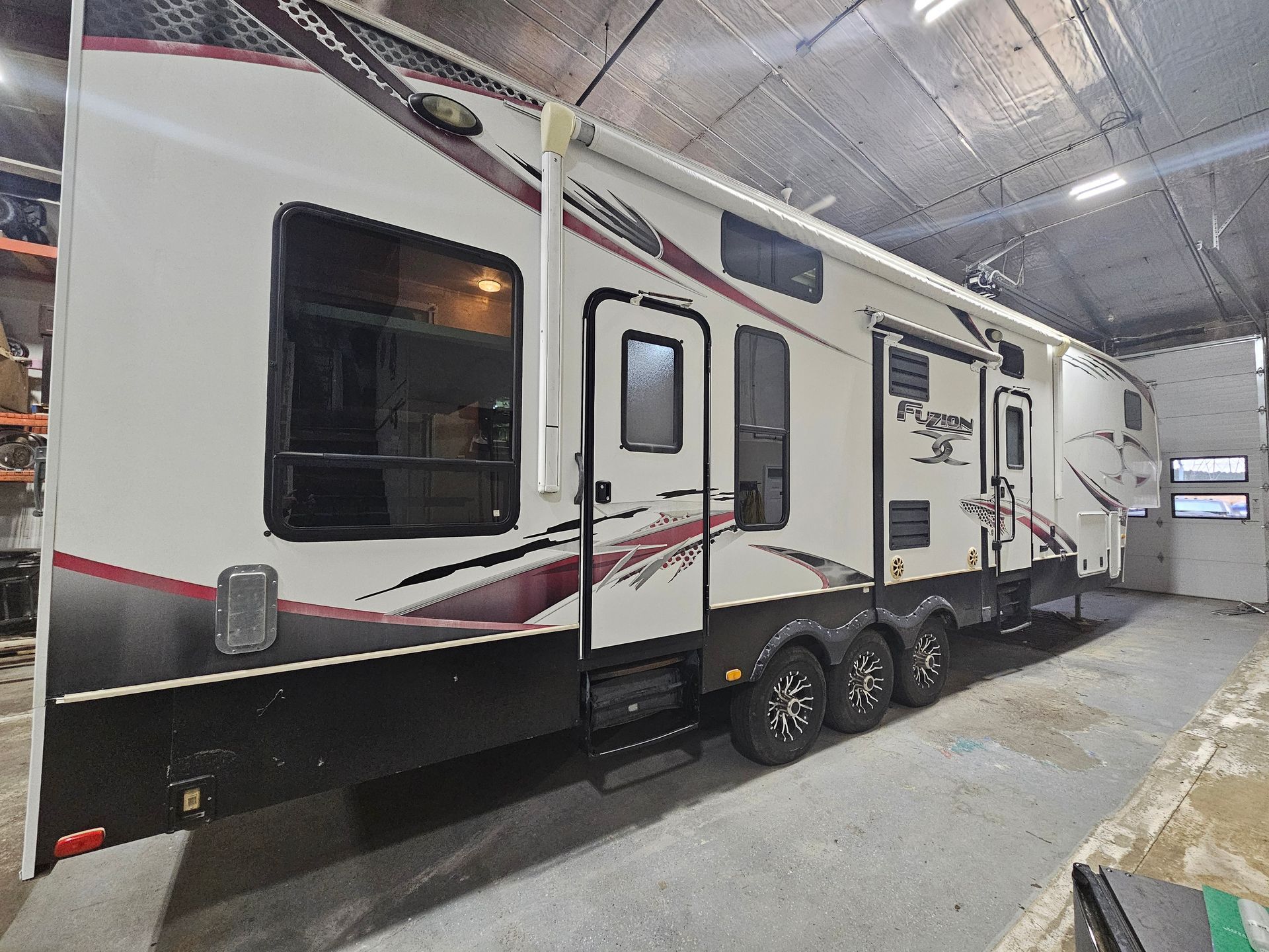 White and black travel trailer with red accents parked indoors in an RV storage bay