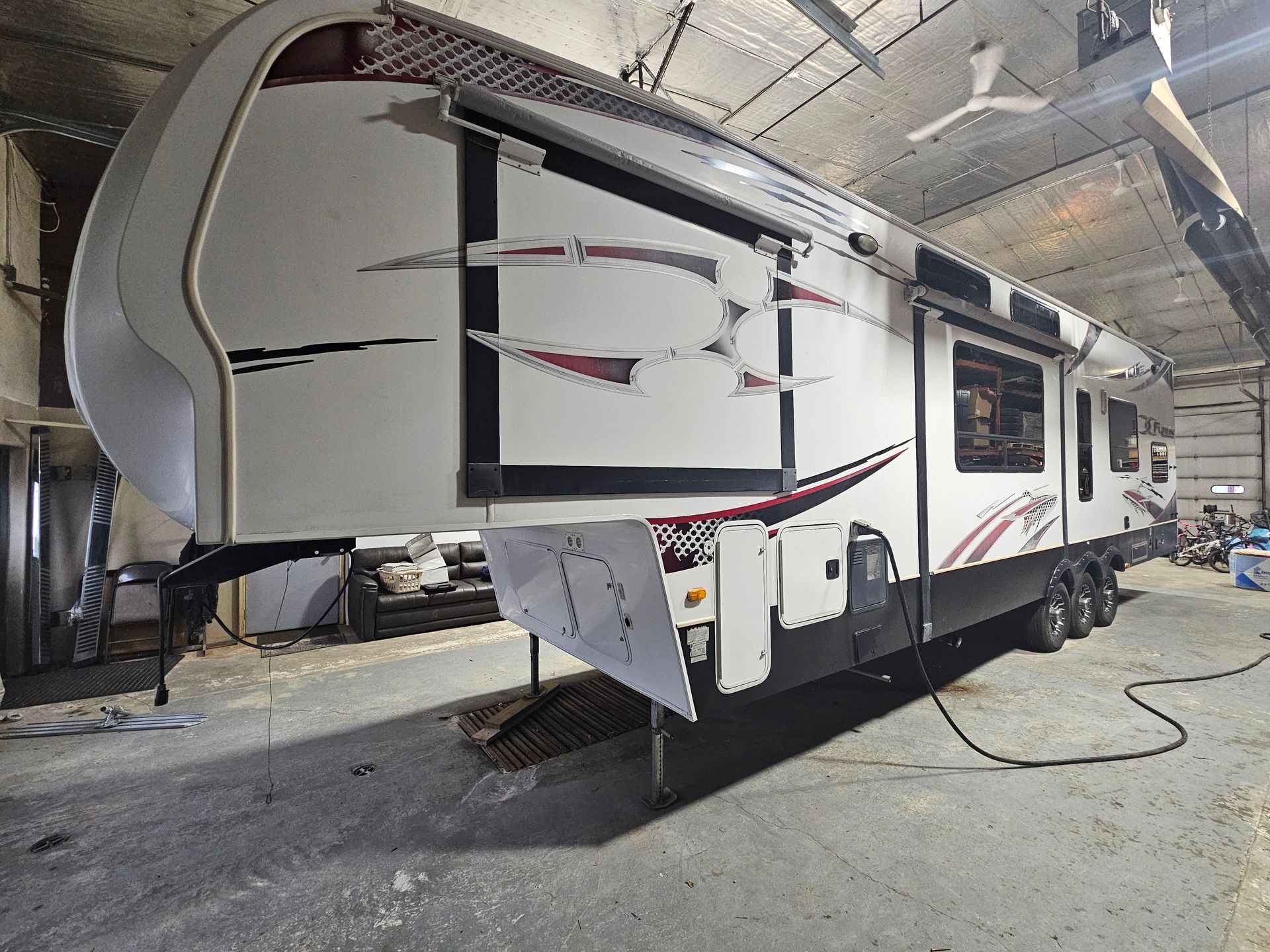 White travel trailer inside a repair shop, front corner damaged and wrapped with straps.