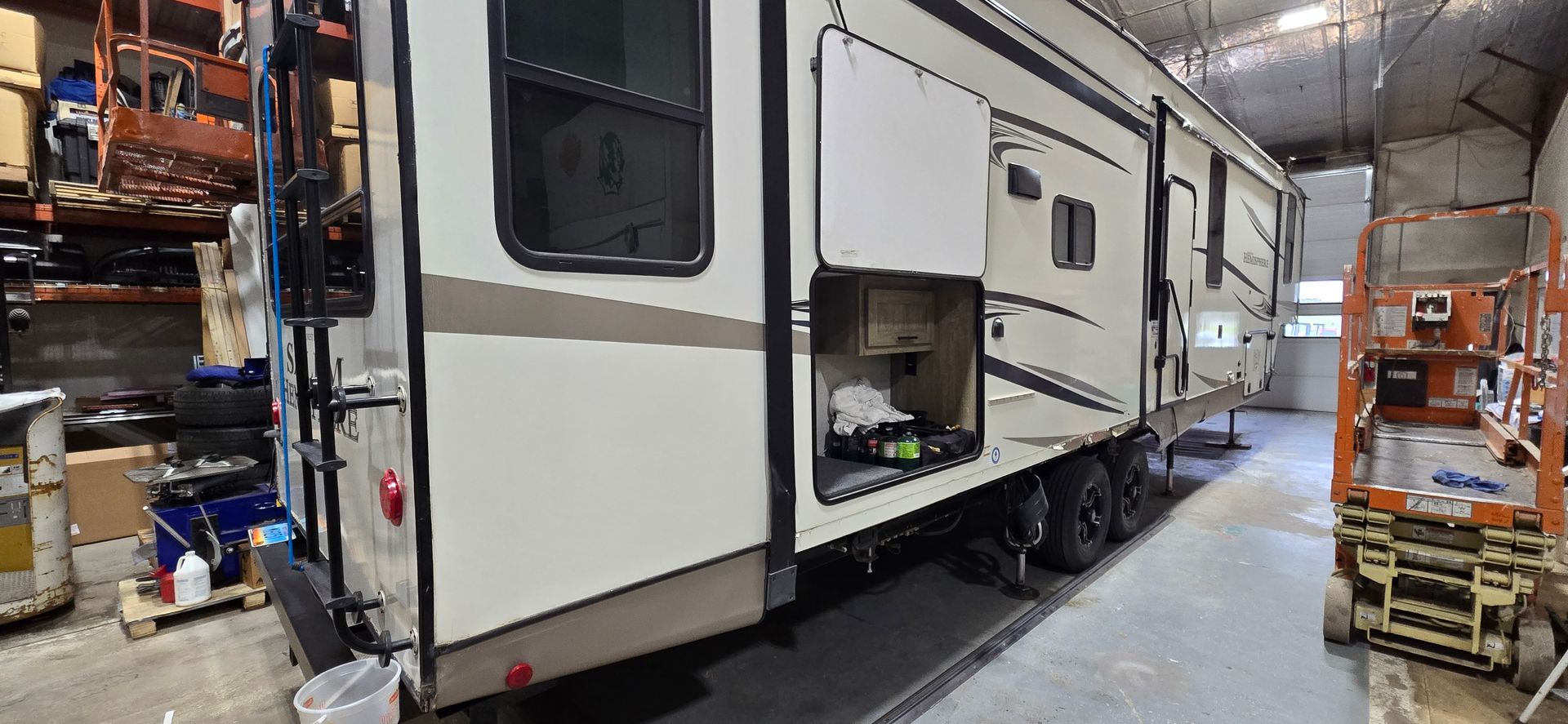 Large white RV trailer inside a warehouse aisle, with storage racks and equipment around it.