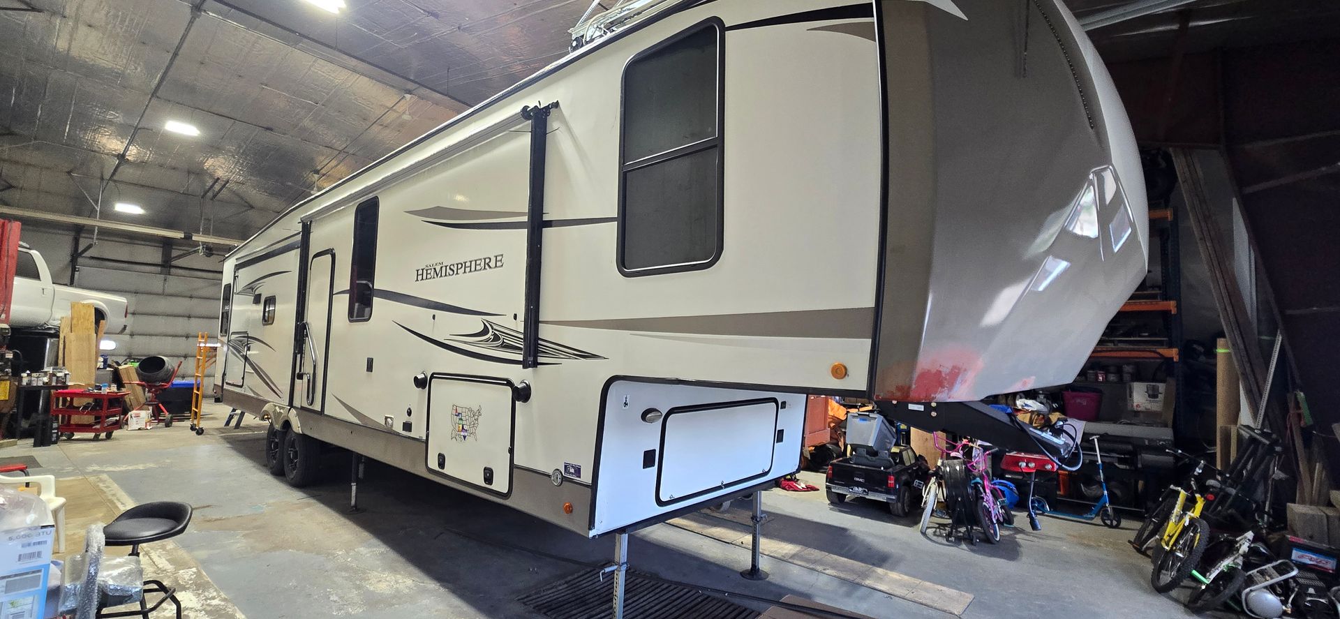 Large white RV parked in a workshop, with an open compartment and tools nearby.