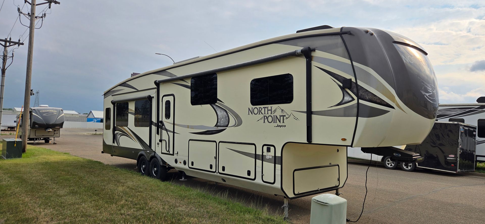 Large beige and gray fifth-wheel RV parked on a roadside under cloudy skies