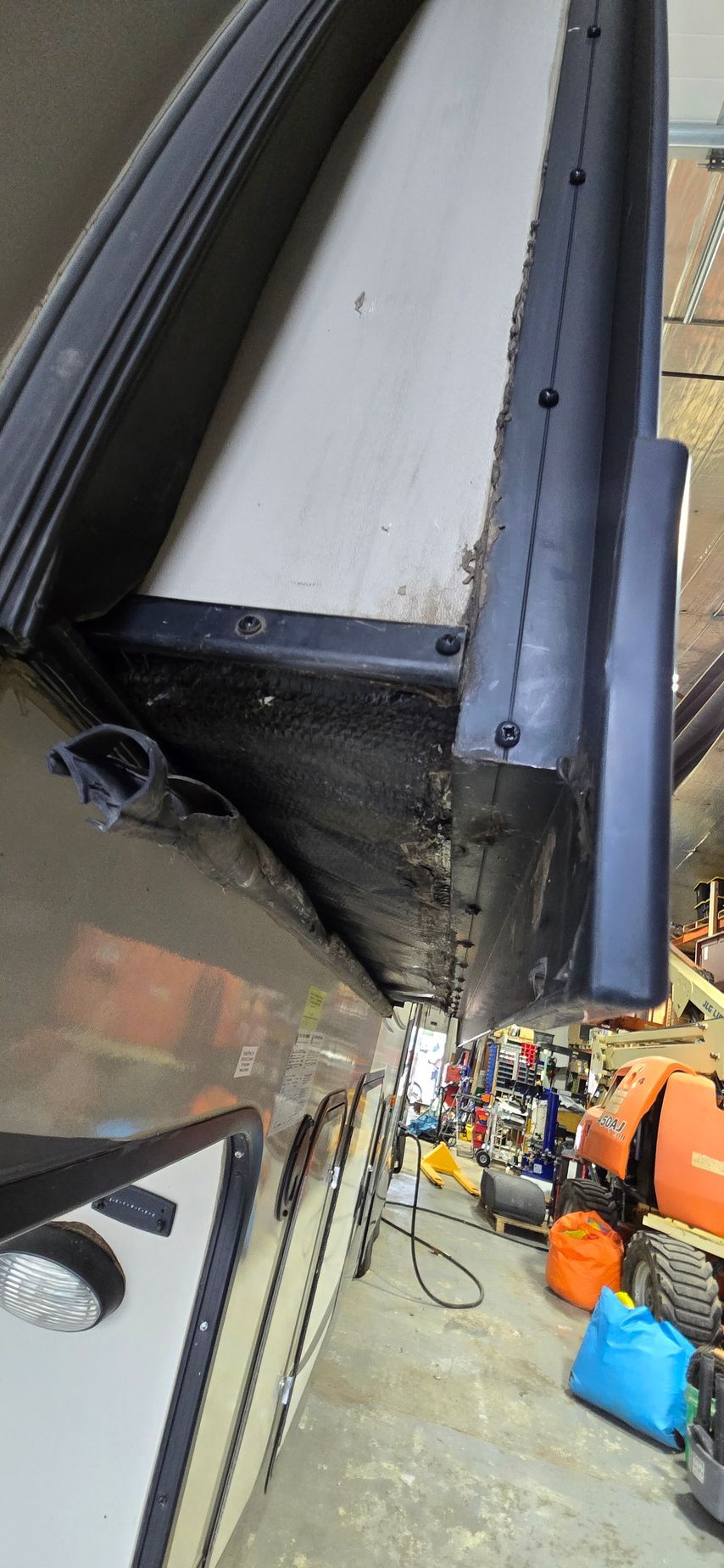 Close-up of a black and white boat hull inside a workshop, with tools and equipment below