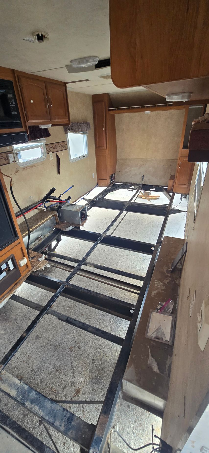 Damaged RV interior with missing floor panels and exposed framing in a cramped hallway