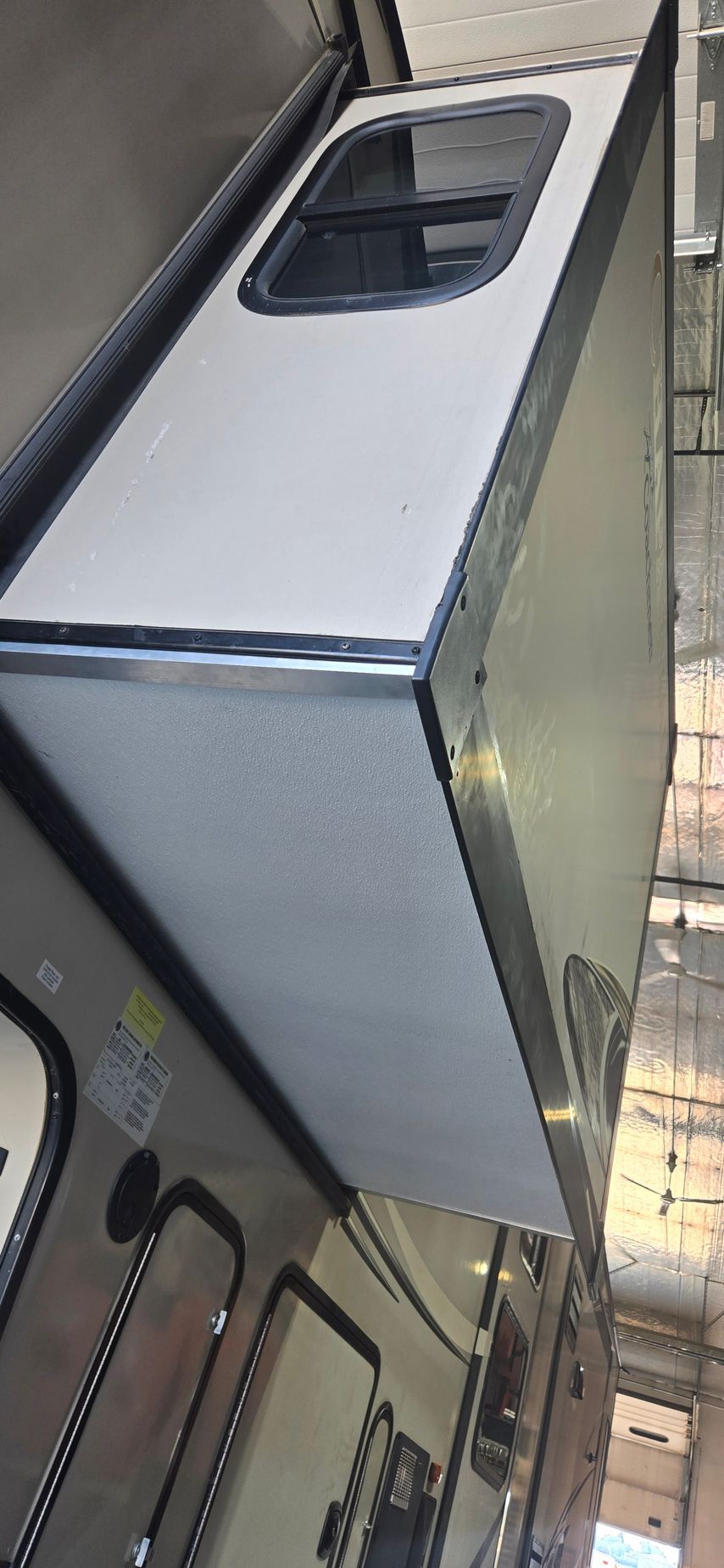White trailer or cargo box with a small window, shown at an angle inside a warehouse setting