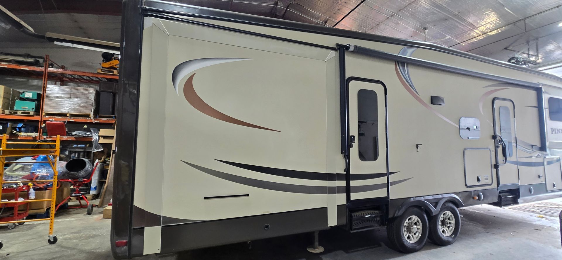 Beige travel trailer with brown swoosh decals parked inside a garage or workshop.