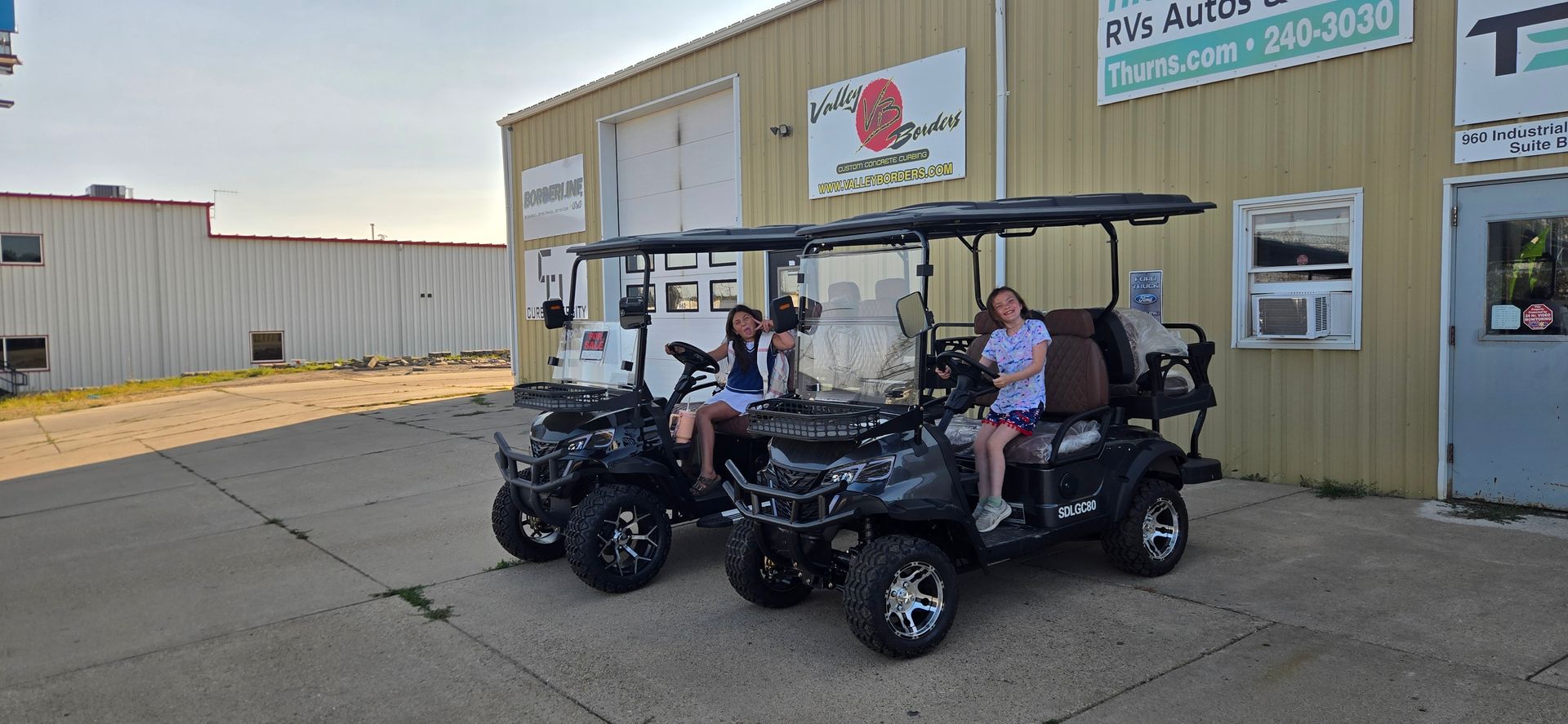 Two people sitting in a black golf cart outside a commercial building.