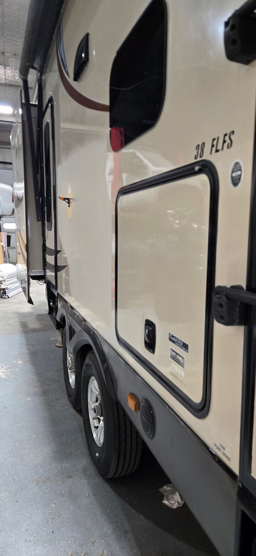 Side view of a beige RV camper parked in a narrow outdoor lot.