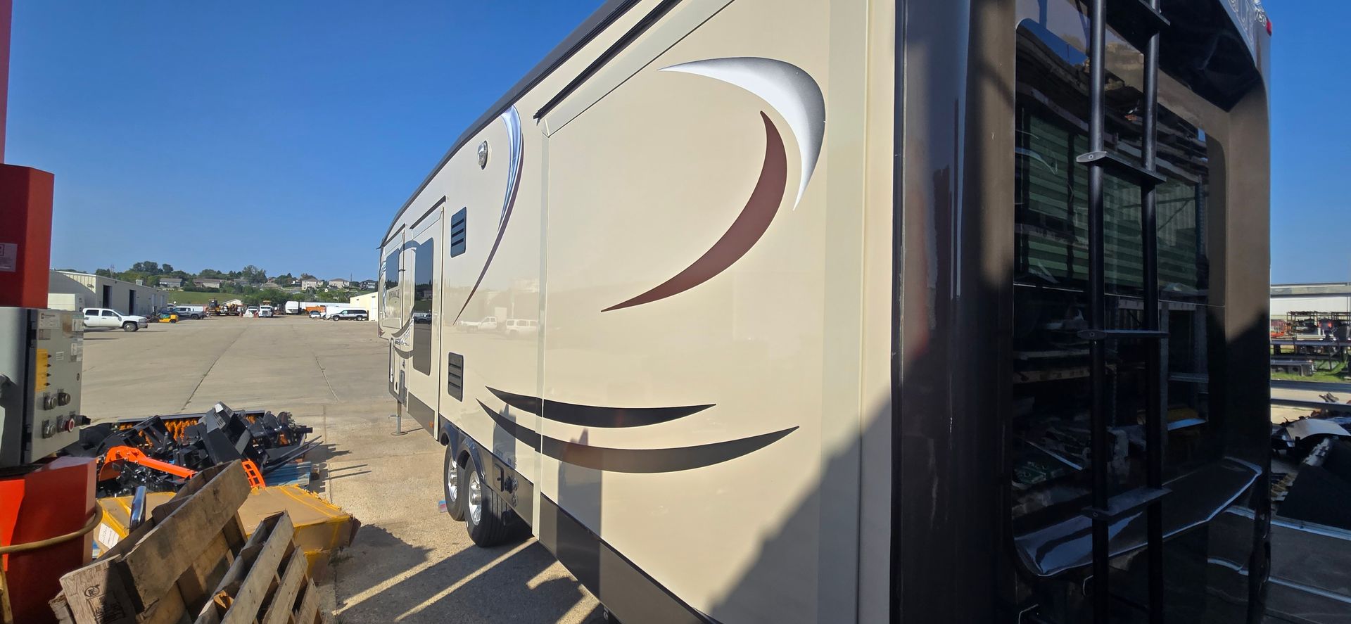 Beige RV trailer parked outdoors beside a building, with steps and cargo nearby.