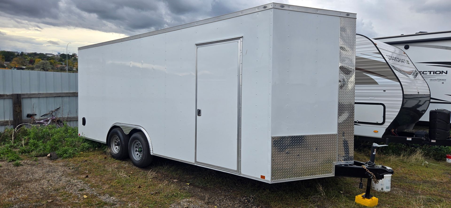 White enclosed cargo trailer with tandem wheels parked outdoors on gravel.