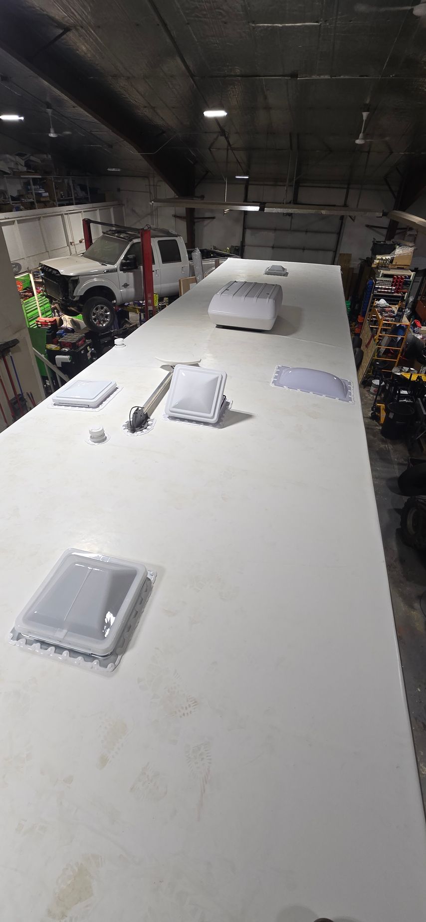 Long white worktable in a workshop with scattered tools and small parts under dim lighting