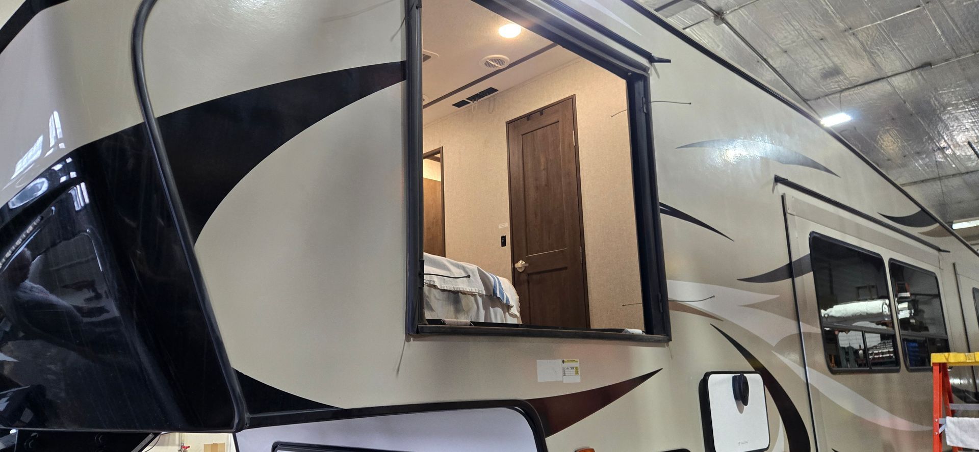 White RV camper with beige accents and an open side window at a dealership or lot