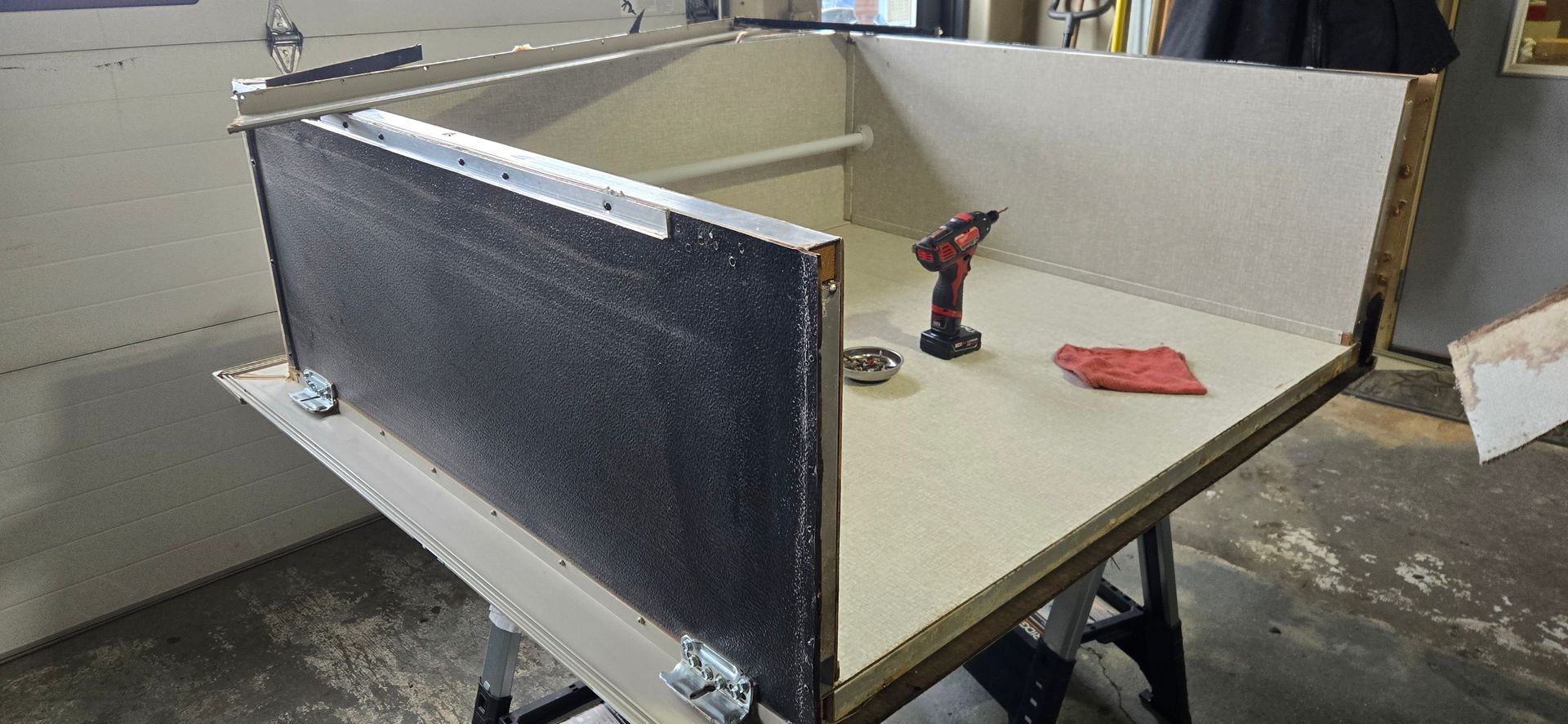 Workbench with beige tabletop, black side panel, and a red power drill in a workshop.