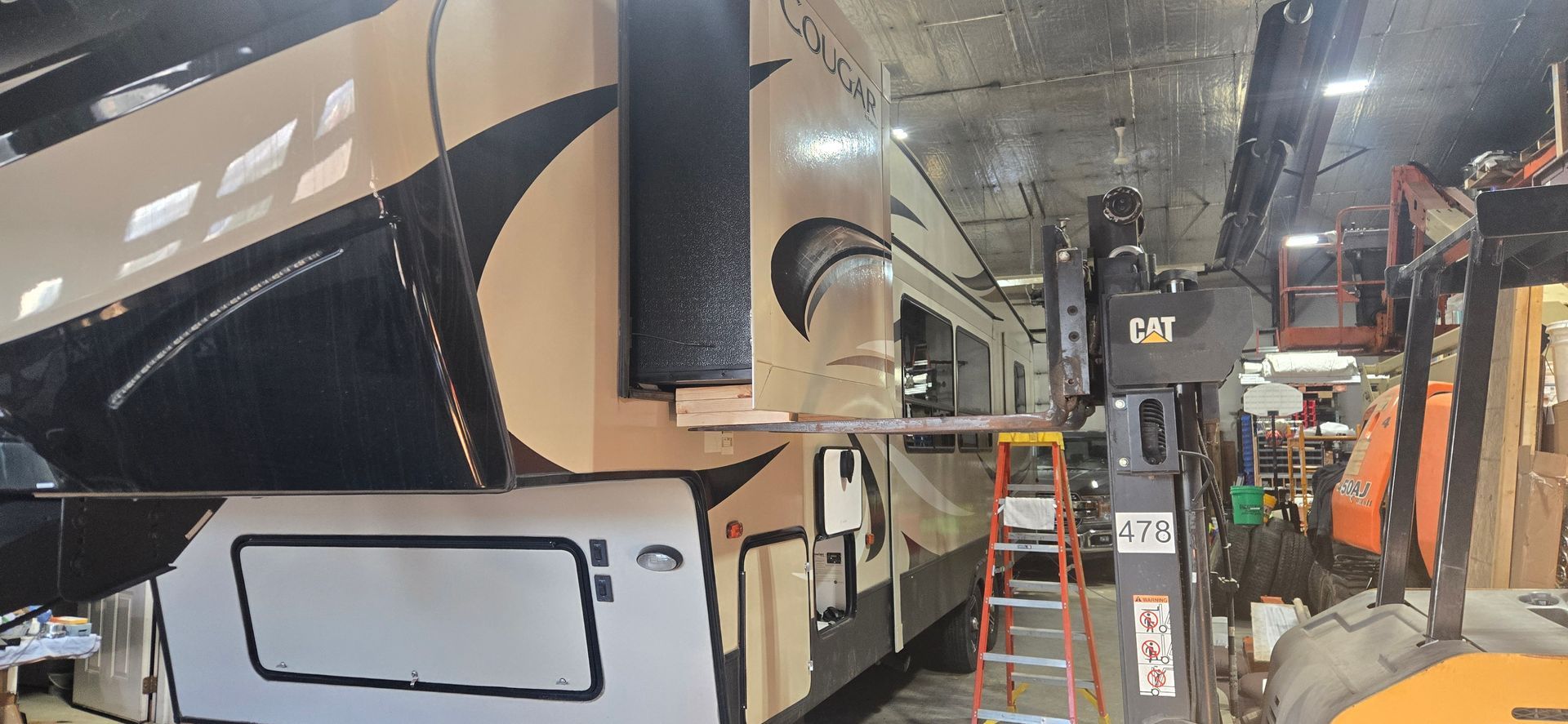 Large black bus or RV parked indoors in a workshop with ladders and equipment nearby