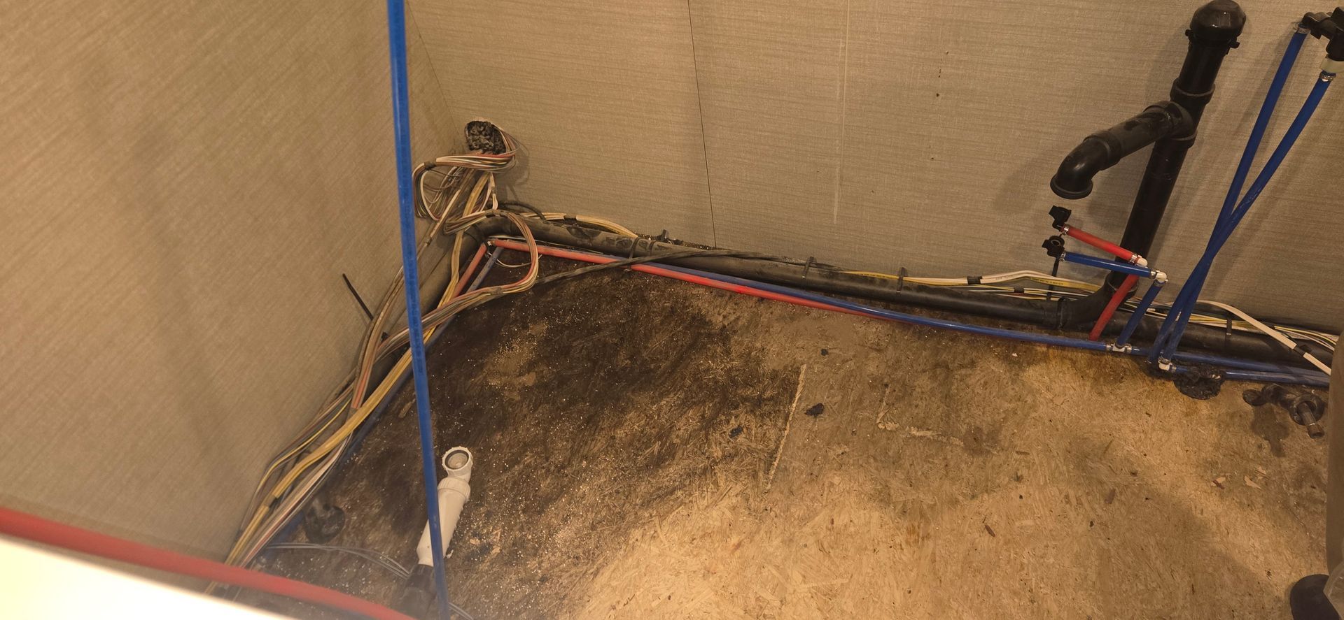 Dirty corner with exposed wiring, blue poles, and a stained floor beside a wall.