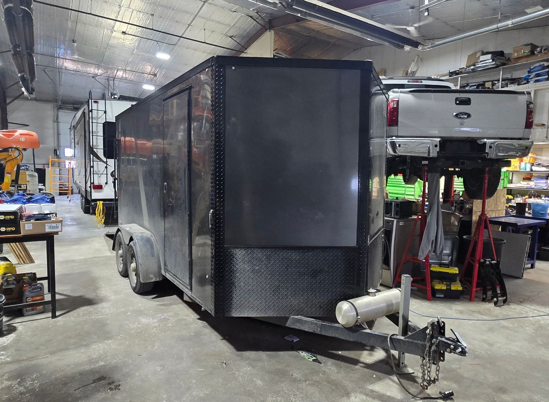 Black enclosed trailer in a workshop, with a white RV and tools nearby