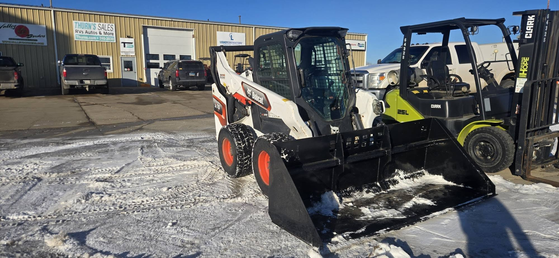 Two skid steer loaders parked on a snowy lot outside a warehouse