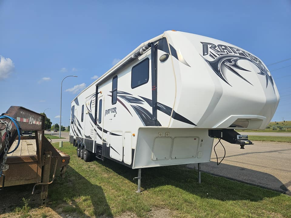 White fifth-wheel RV parked beside a roadside with a blue sky overhead