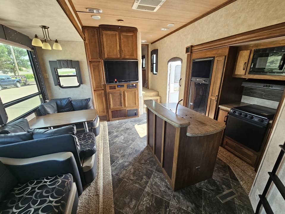 RV interior with sofa, dinette, and kitchen cabinets in a wood-paneled living space