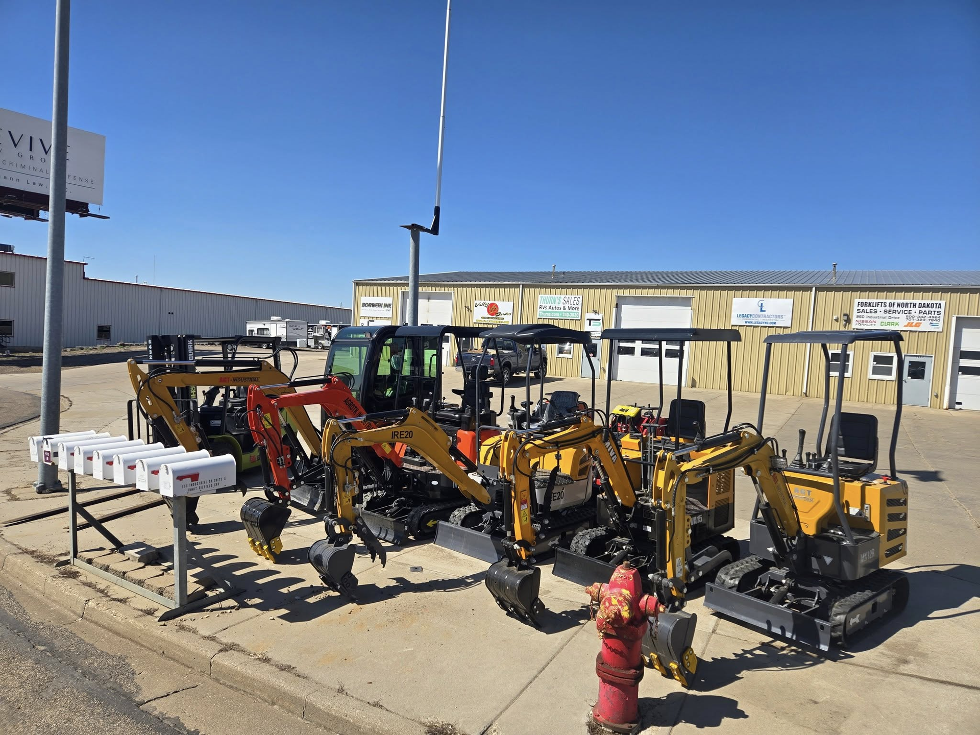 Yellow backhoes and construction equipment parked in a row beside a red fire hydrant on a sunny lot