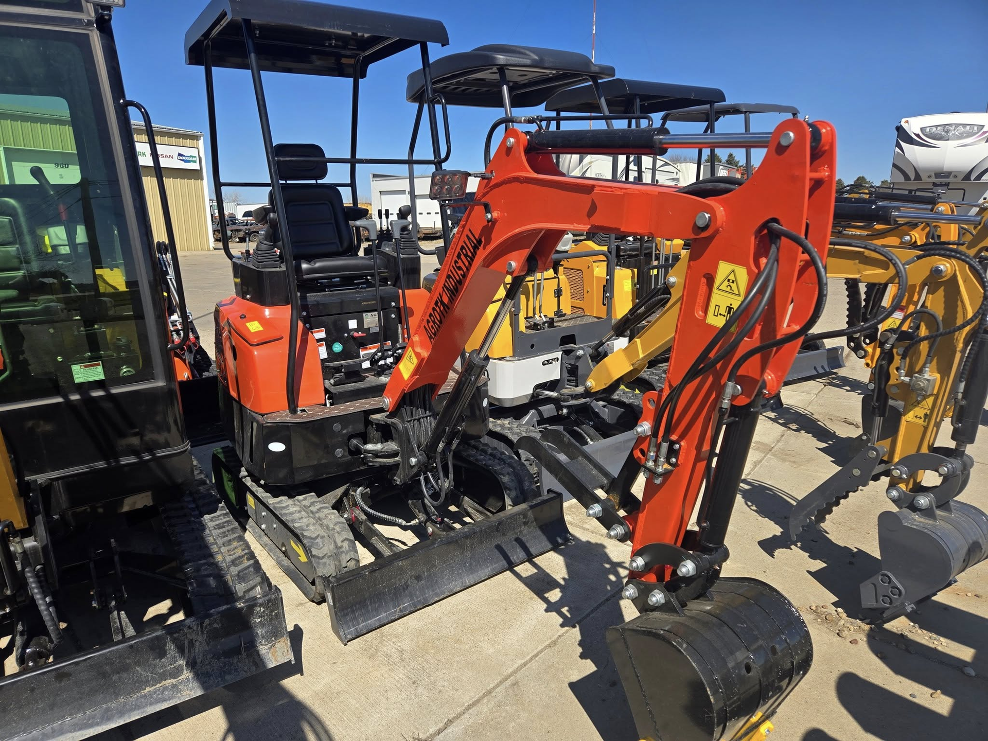 Orange compact excavator with front loader attachment parked on a lot next to other construction machines