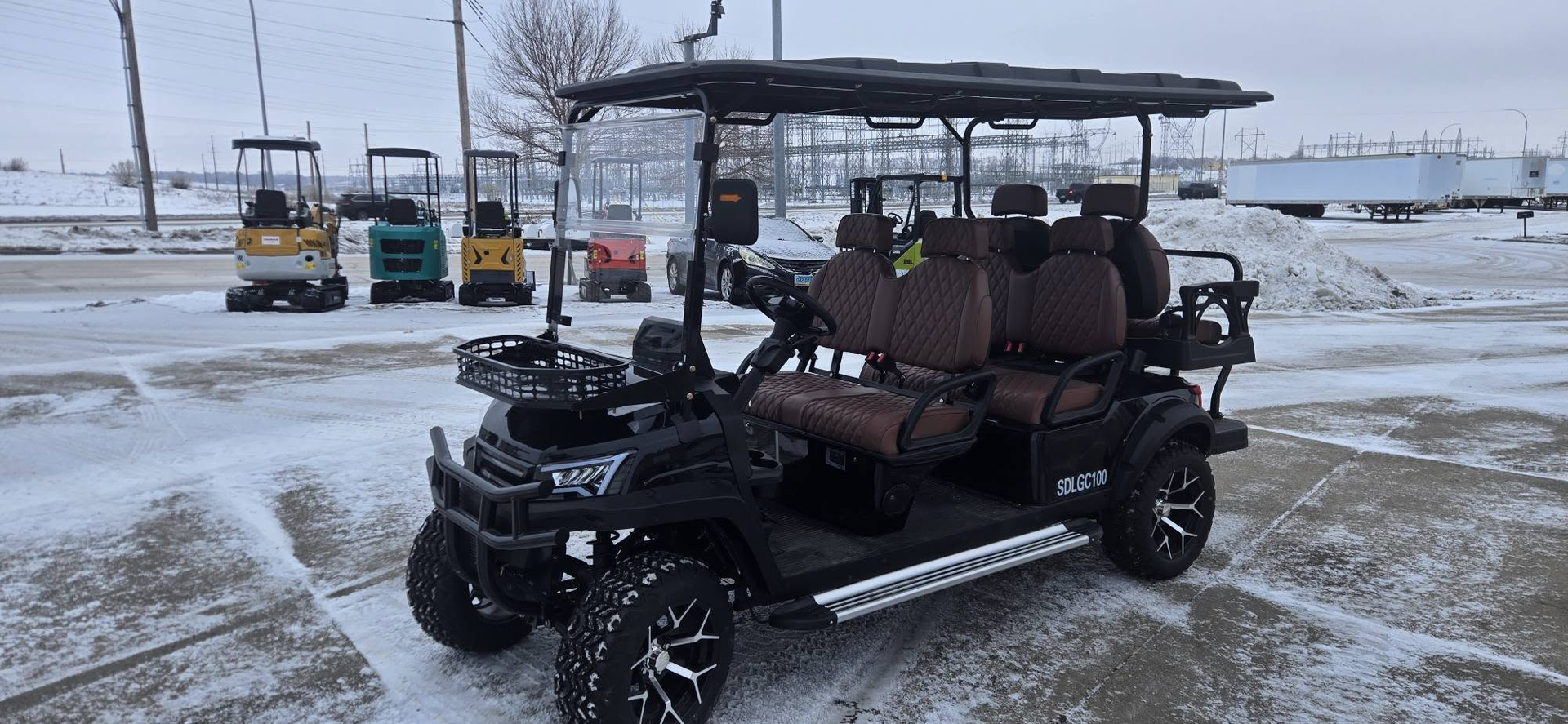 Black off-road golf cart with a canopy and brown seats parked in a snowy lot near other carts