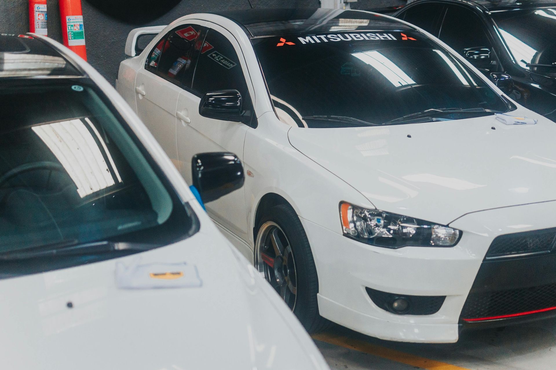 Two white sports cars parked indoors, one with a black hood and windshield banner