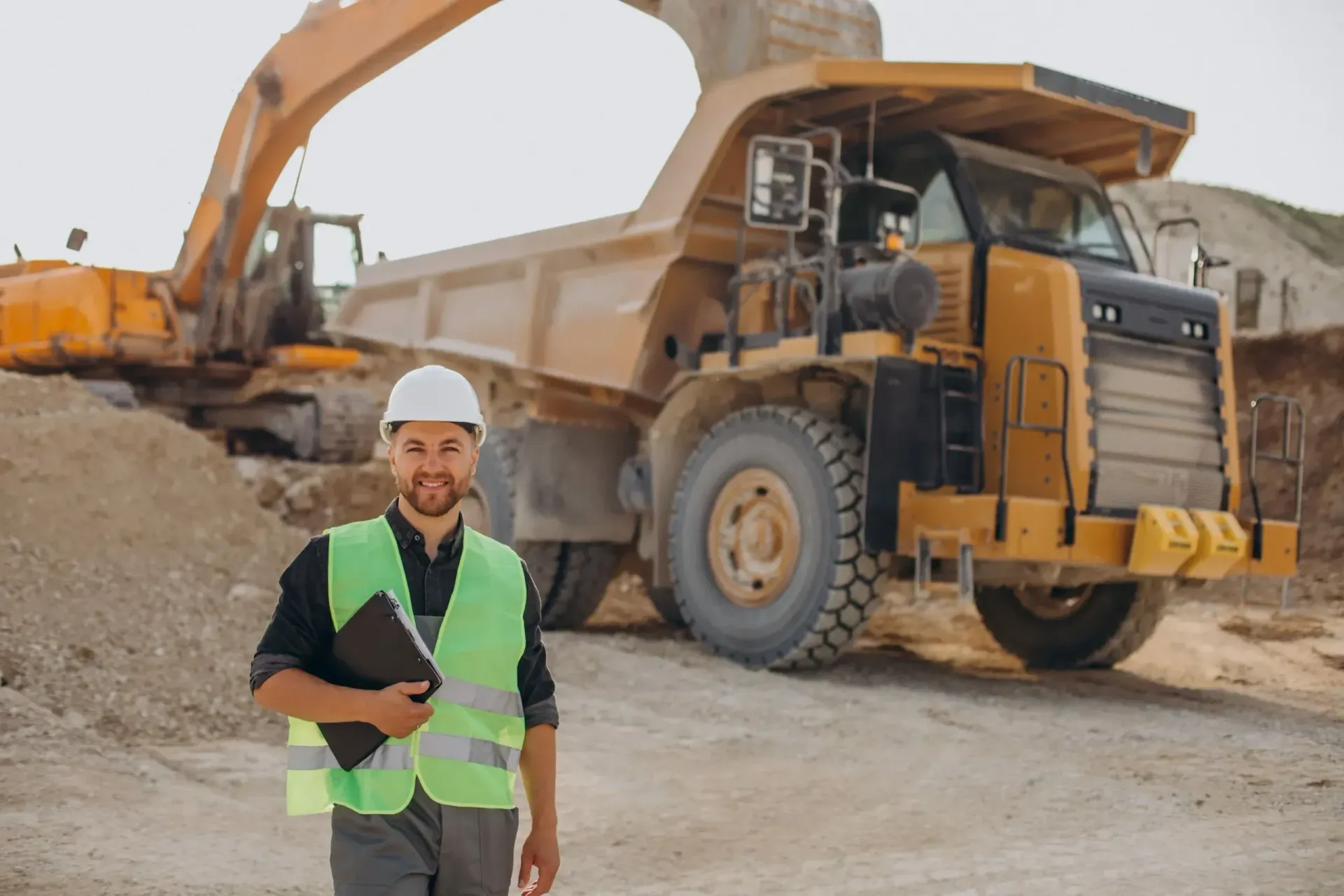 Operário da construção civil com colete de segurança e capacete em pé diante de um caminhão basculante .