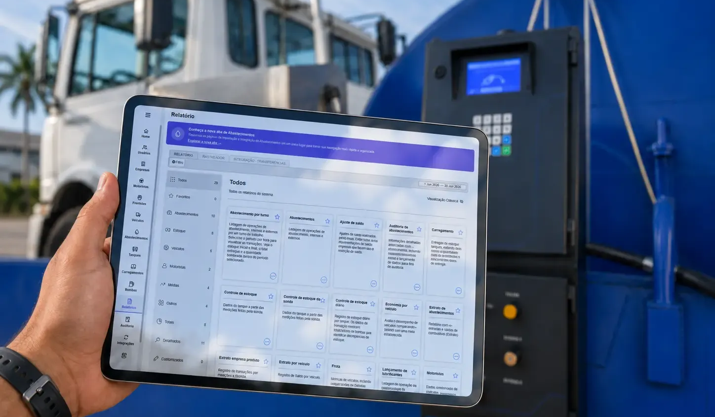 Mão segurando um tablet com um painel de controle ao lado de uma máquina industrial azul ao ar livre