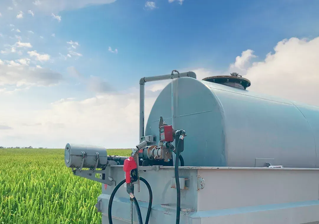 Dois trabalhadores inspecionam um grande pulverizador agrícola cinza em um campo verde sob um céu azul.