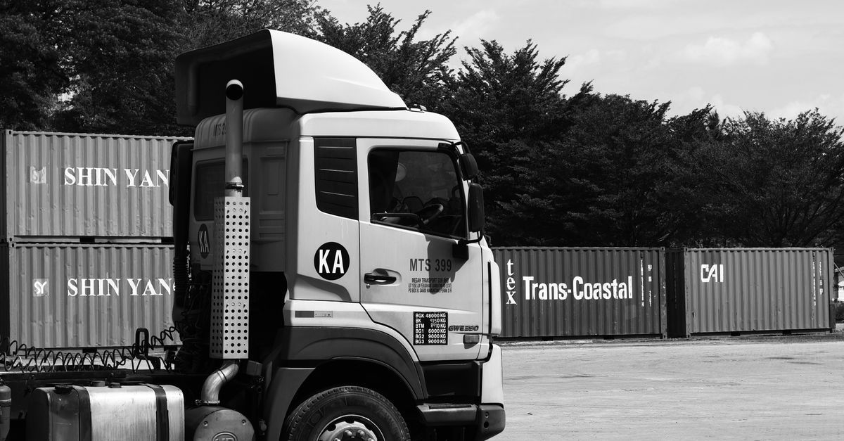Bomba de diesel ao lado de tanque de armazenamento em pátio de frota com caminhões estacionados.