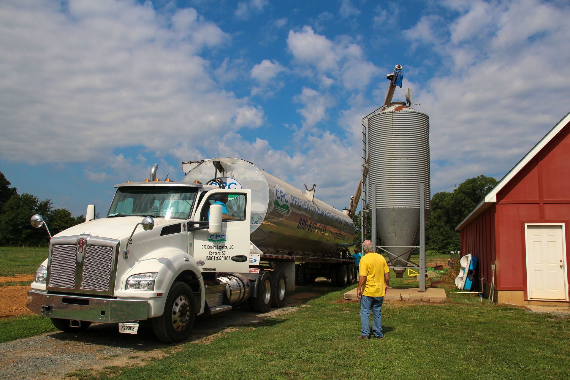 Caminhão-tanque prateado ao lado de um silo de grãos em uma fazenda.