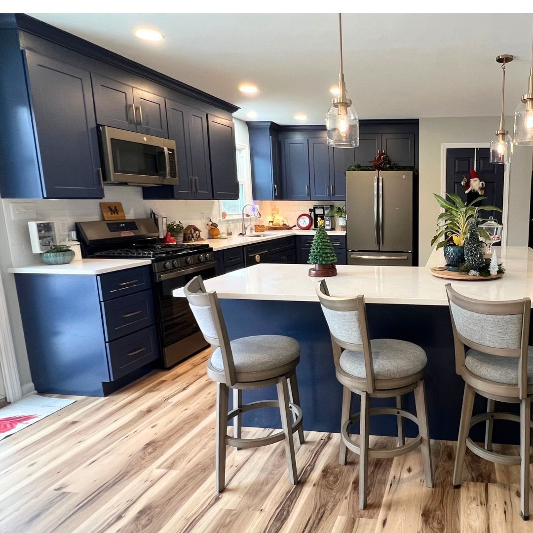 Modern kitchen with navy cabinets, white island, bar stools, stainless appliances, and pendant lights