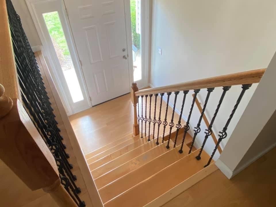 Staircase with light wood steps, black iron railing, and a front door with sidelights at the bottom.