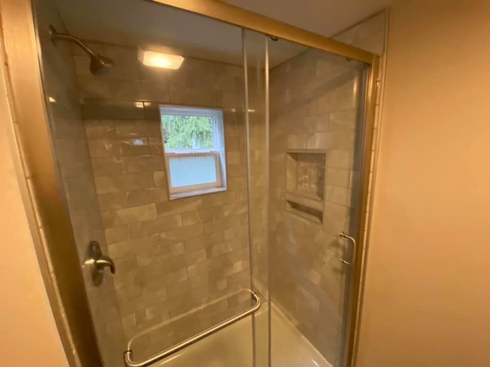 Glass shower stall with beige tile walls, chrome handles, and a small window inside.